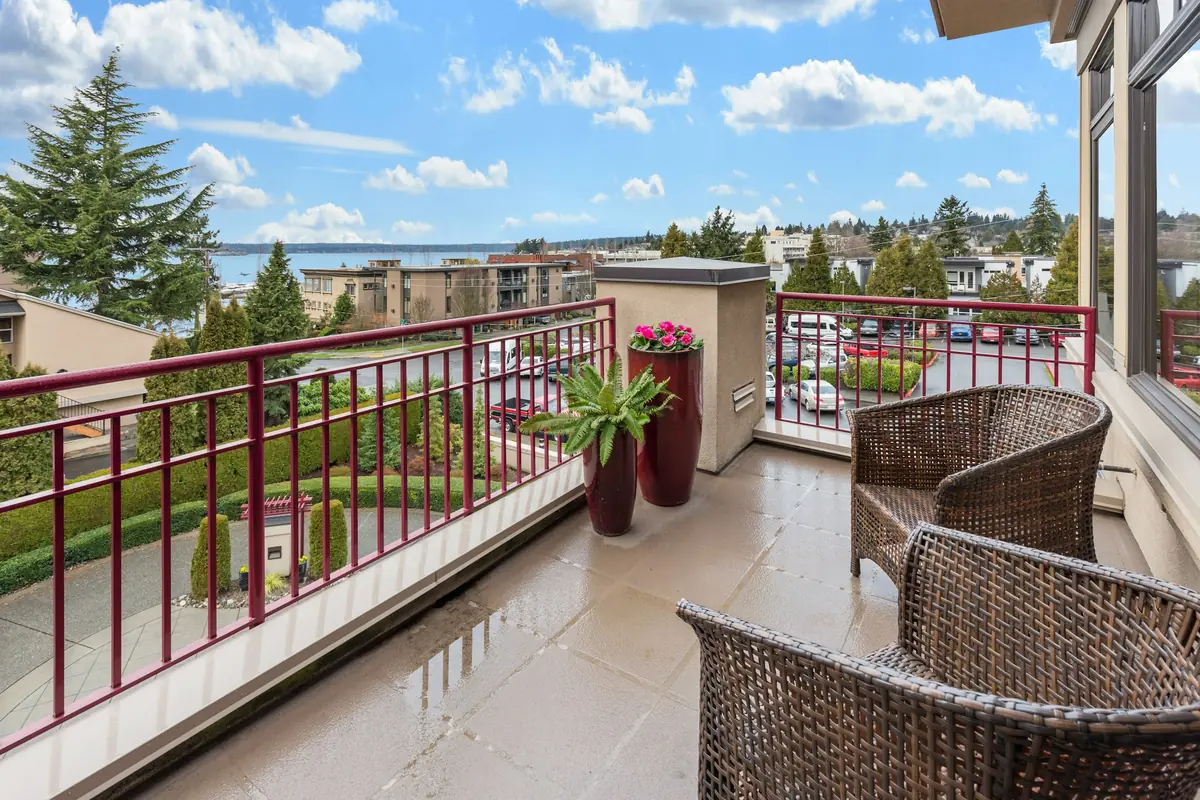 Wicker armchairs and potted plants on a wet condo balcony with red metal railings