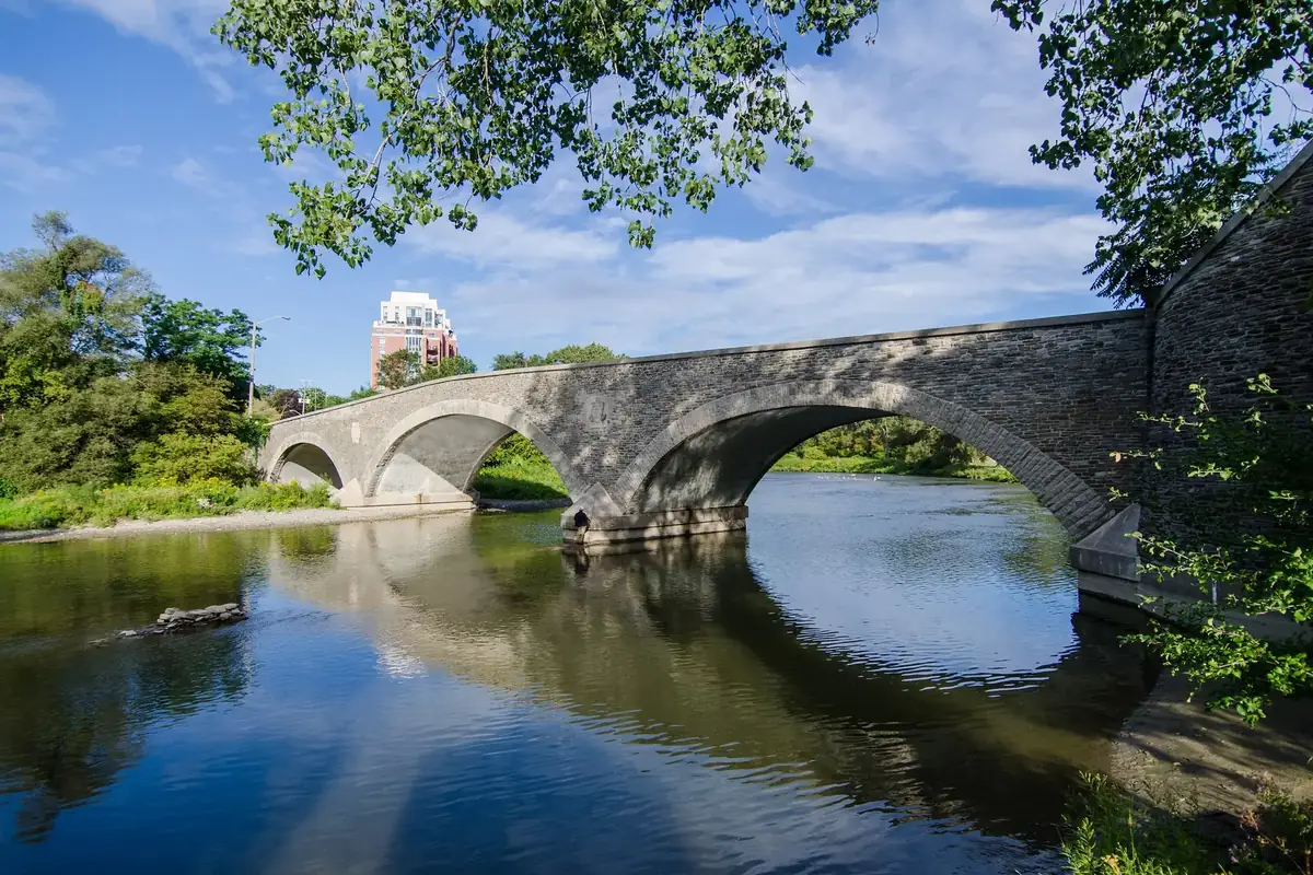 Stone arches of the Old Mill Bridge reflected in the Humber River at the western edge of Bloor West Village, Toronto