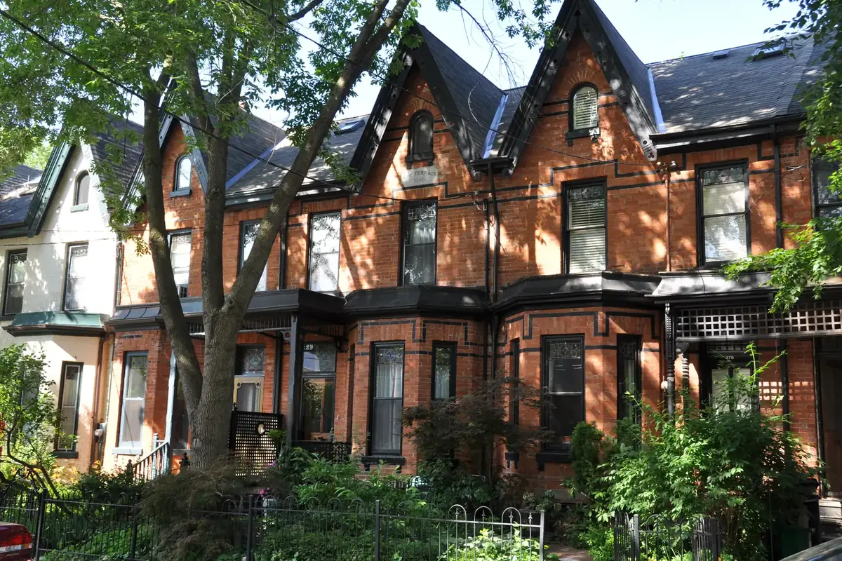 Row of Victorian bay-and-gable brick houses under shady street trees in Cabbagetown, Toronto