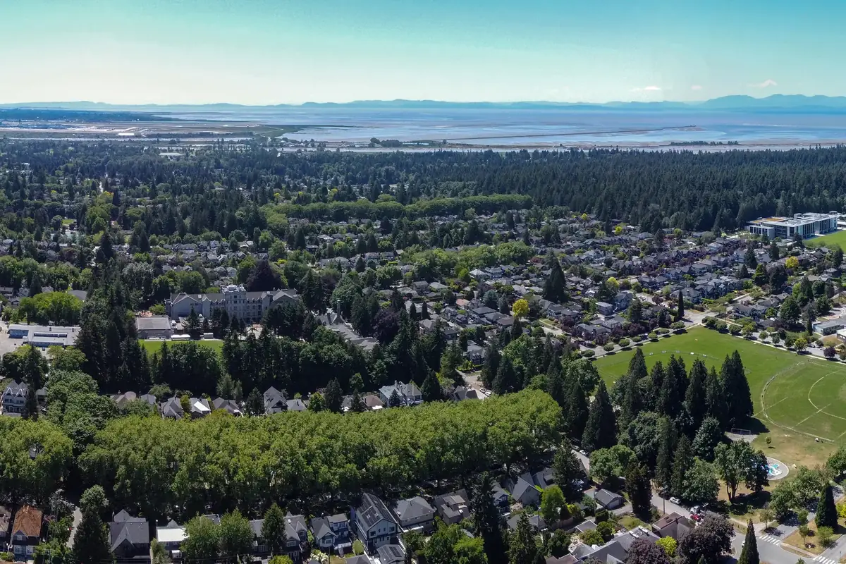 Aerial view of Dunbar–Southlands, Vancouver: leafy streets of family homes and a neighbourhood park, with Pacific Spirit Park’s forest and the Fraser River estuary beyond