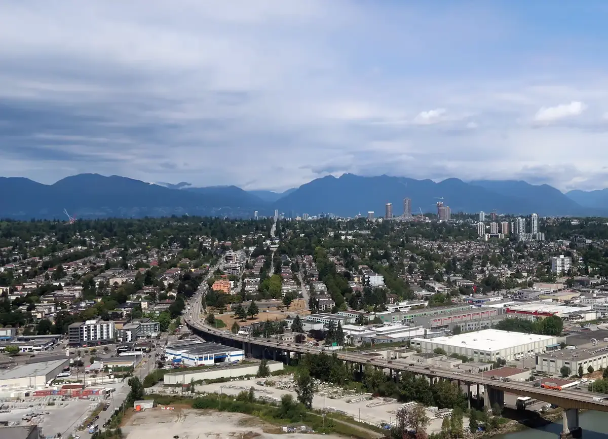 Aerial view of Marpole’s streets beside the Fraser River, with the Arthur Laing Bridge and the North Shore Mountains beyond, Vancouver