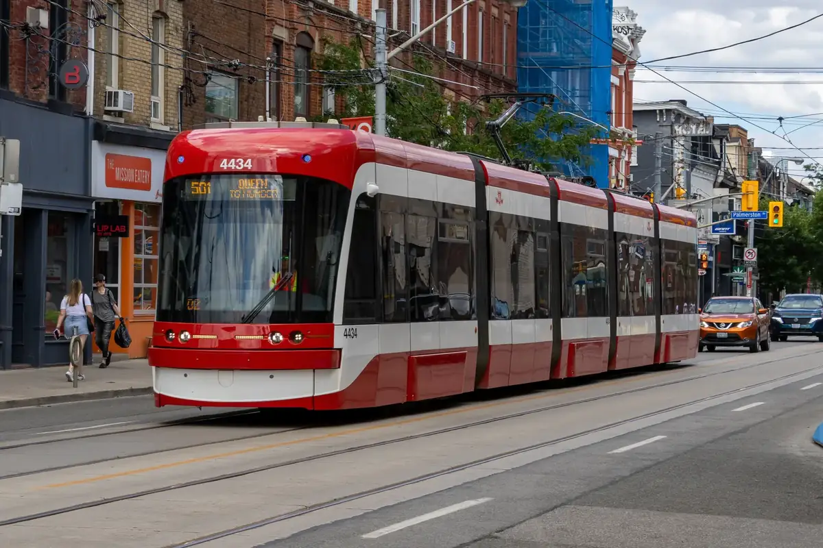 A red 501 Queen streetcar passing Victorian storefronts on a sunny Queen Street West, Toronto