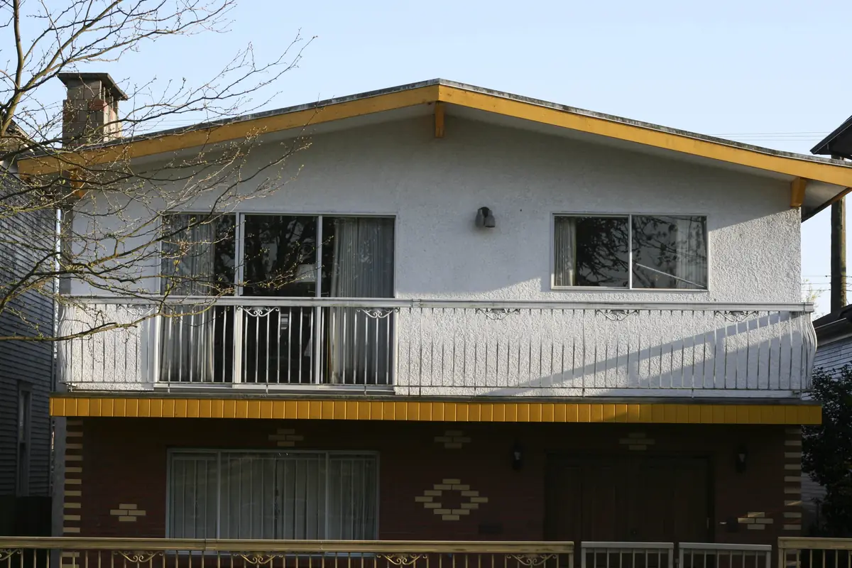 A Vancouver Special house with a stucco upper floor, a long balcony and a brick ground floor, Vancouver