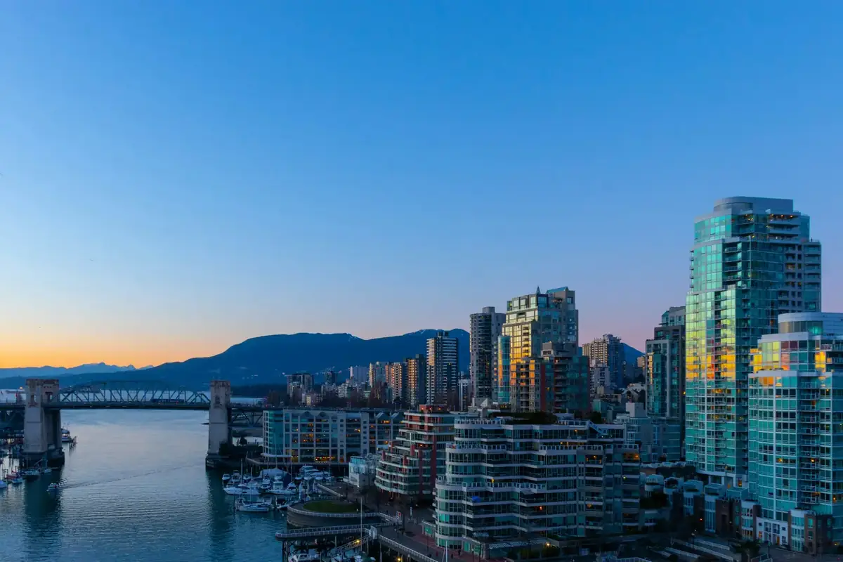 West End apartment and condo towers over False Creek at dusk, with the Burrard Bridge behind