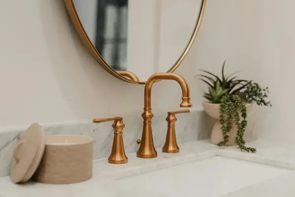 Brushed-brass faucet on a white marble vanity beside a round mirror