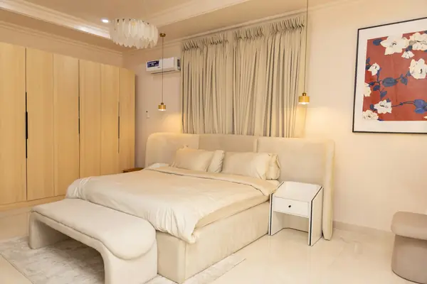 Warm neutral bedroom with a cream upholstered bed, light-oak wardrobes and linen drapes