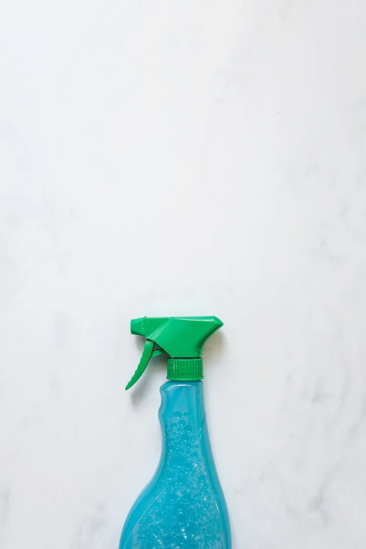 A refillable spray bottle with a green trigger on a white marble surface