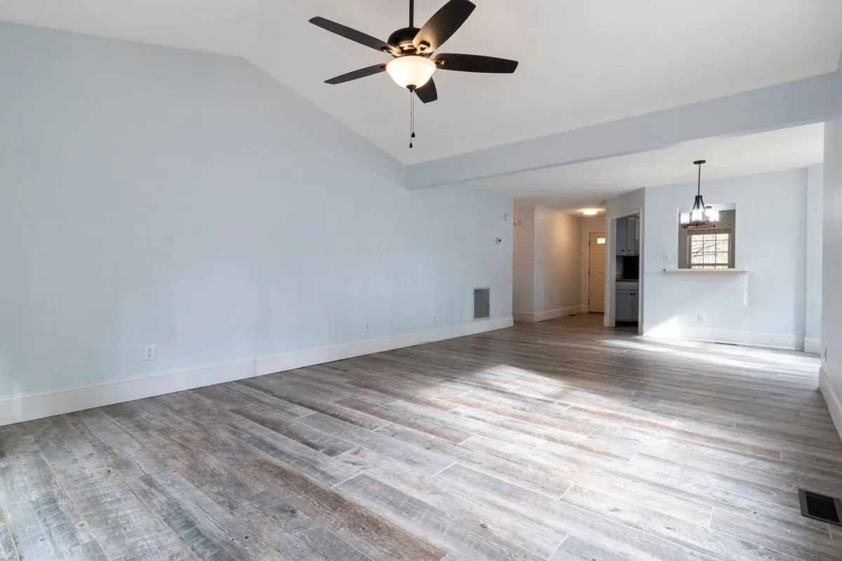 Empty living room with pale blue walls, a grey plank floor and a ceiling fan