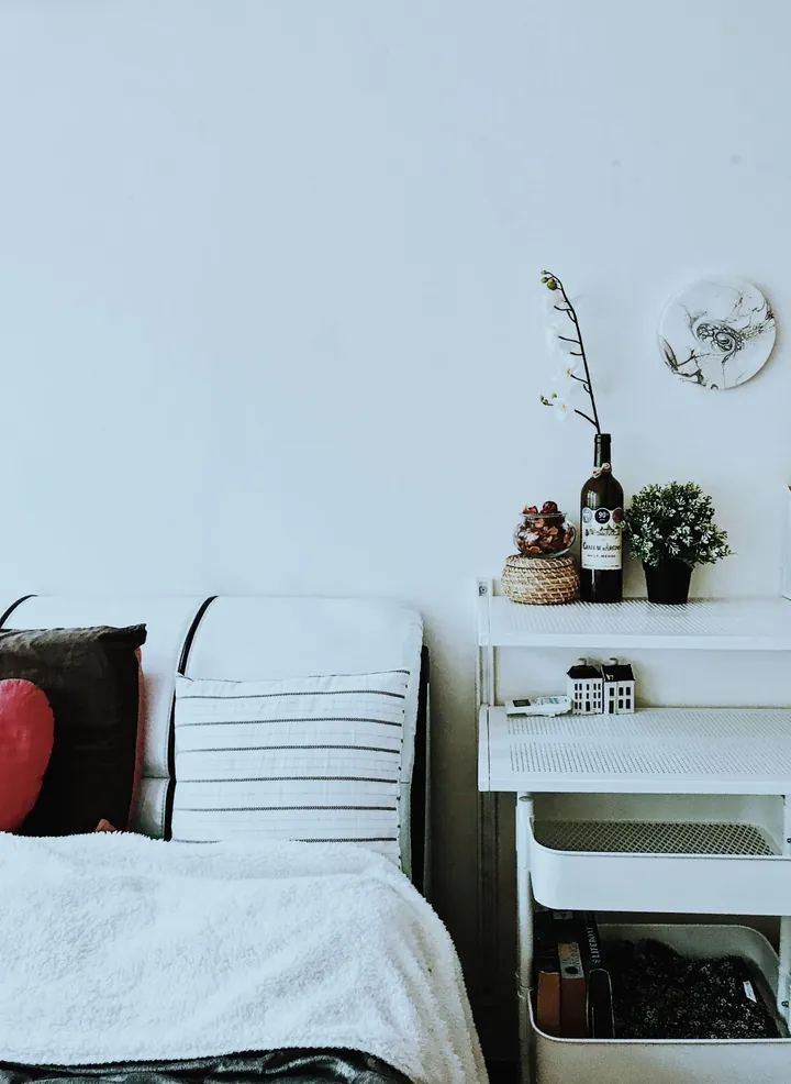 A tidy bedroom corner with a made bed, striped cushions and a white shelving cart