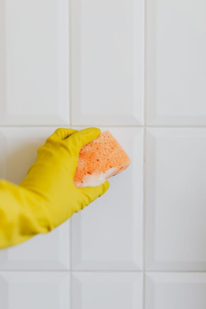 Yellow-gloved hand with sponge cleaning a white tiled wall