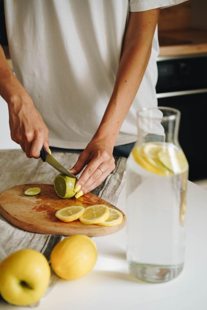 Hands slicing lemons and lime for infused water in a bright kitchen