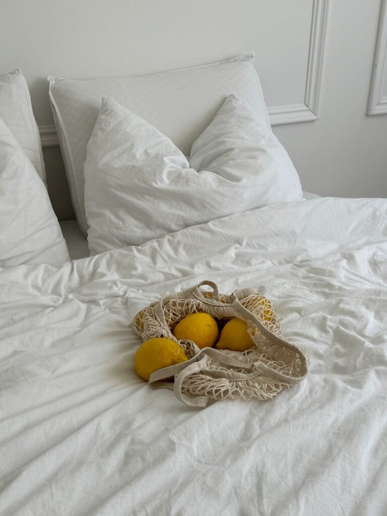 White bed with fluffy pillows and a mesh bag of lemons