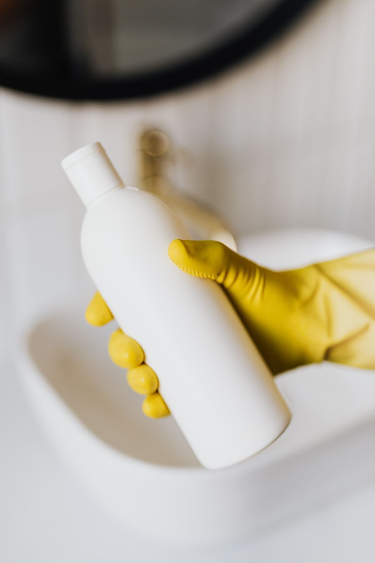Crop person in rubber gloves with white cosmetic bottle -