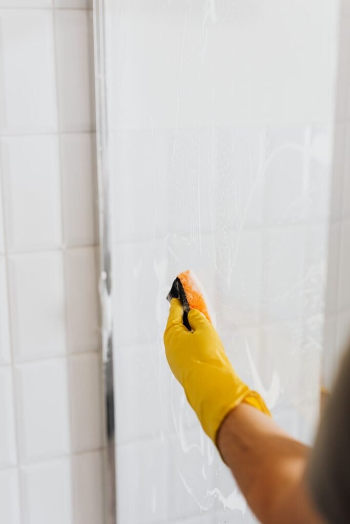 Hand in yellow glove scrubbing a soapy shower door with a sponge