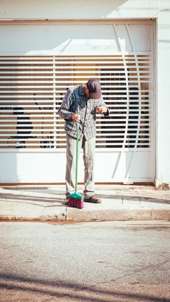 Man sweeping a sidewalk with a broom beside a white gate
