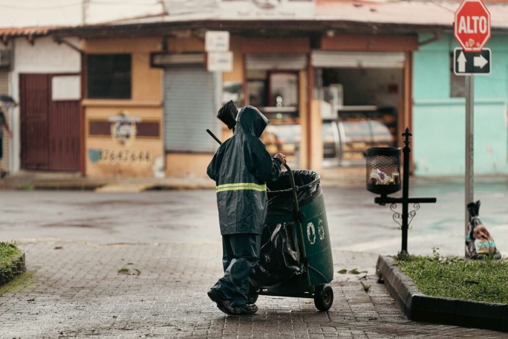 Street cleaner pushing a cart on a wet urban street