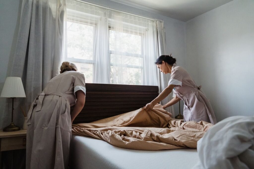 Woman in Brown and White Uniform Fixing Brown Bed Blanket -