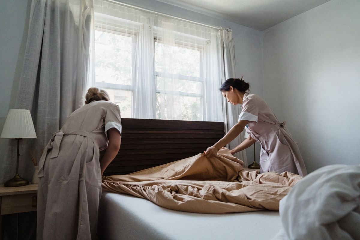Woman in Brown and White Uniform Fixing Brown Bed Blanket -