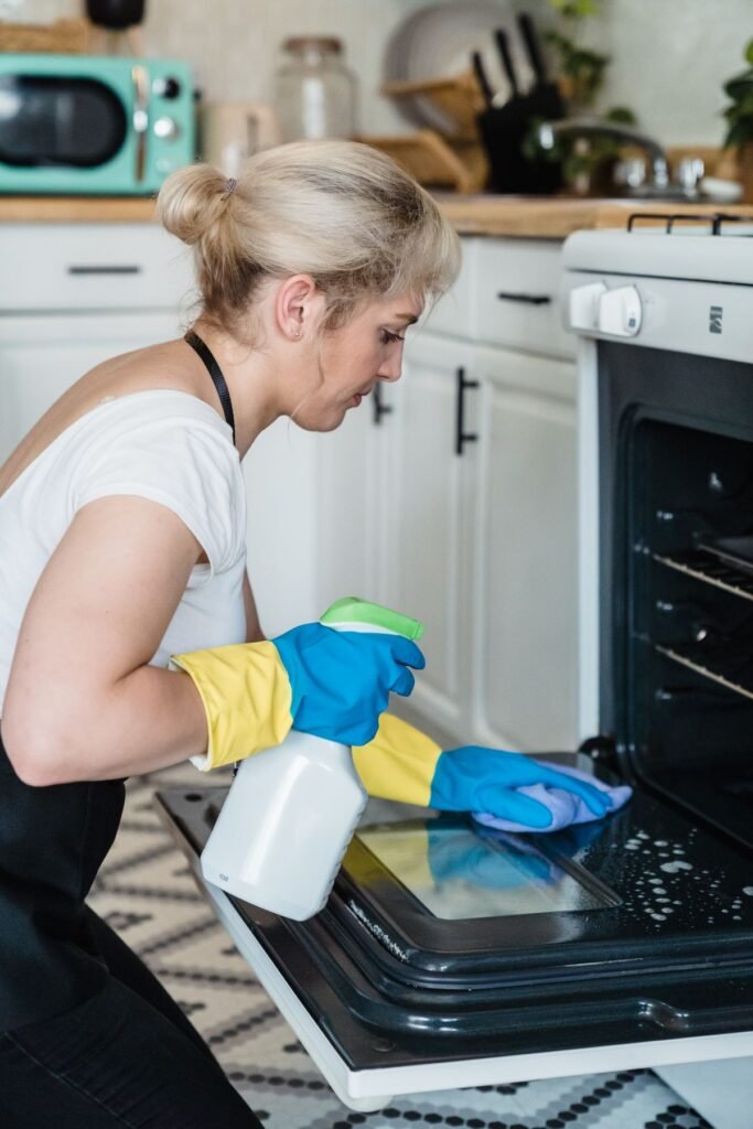 Woman cleaning an oven door with a spray bottle and cloth
