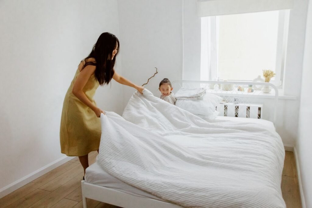 Parent and child making the bed together in a bright, tidy bedroom