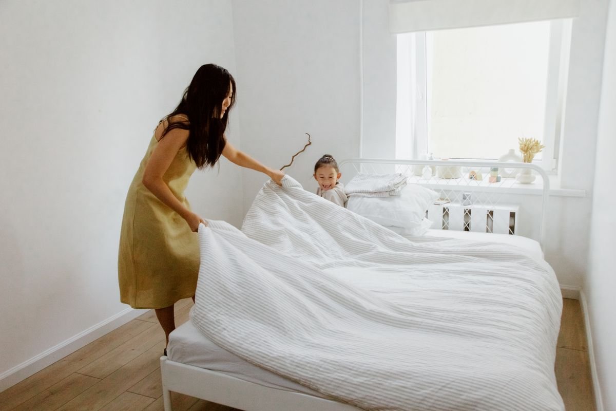 Parent and child making the bed together in a bright, tidy bedroom