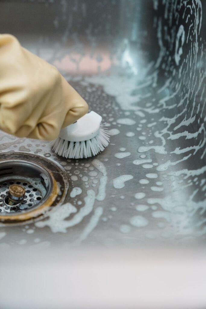 Gloved hand scrubbing a stainless steel kitchen sink with suds